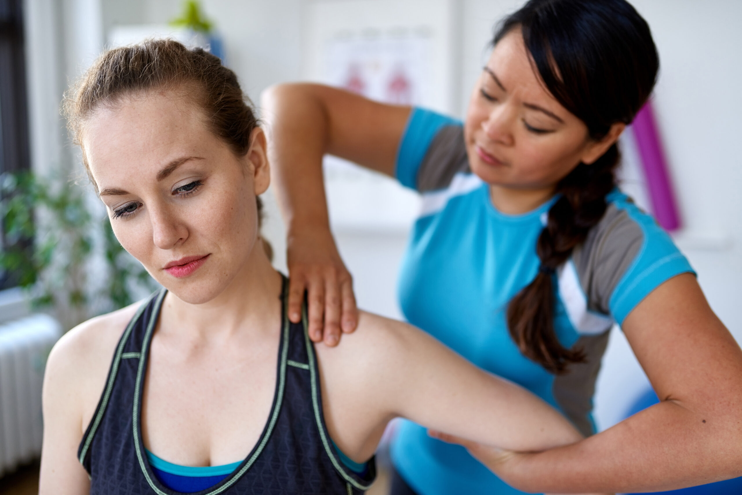 Candid image of an attractive patient during a appointment with professional asian physiotherapist in design kinesio clinic working and massaging her neck and shoulder pain